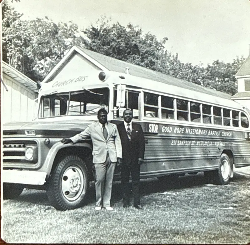 Archival photo of two men in suits standing in front of a church bus lettered Good Hope Missionary Baptist Church, 821 Sampson St., Westlake, LA
