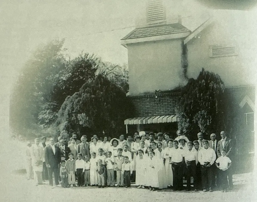 Archival photo of a large group of church members of all ages gathered outdoors in front of the church building