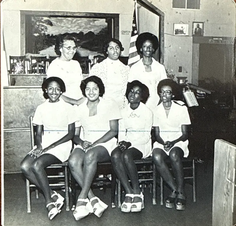 Archival photo of seven women dressed in white, four seated and three standing, inside the church